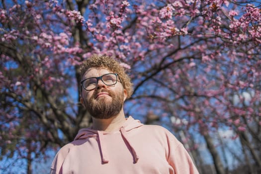 Man allergic enjoying after treatment from seasonal allergy at spring. Portrait of happy bearded man smiling in front of blossom tree at springtime. Spring blooming and allergy concept. Copy space.