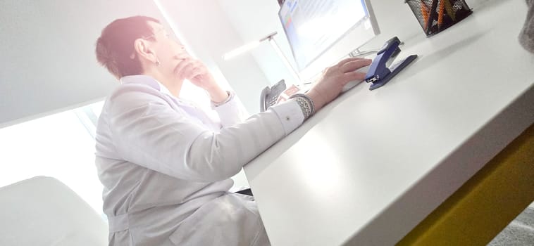 doctor sits at the table and looks at tests on the computer, family doctor