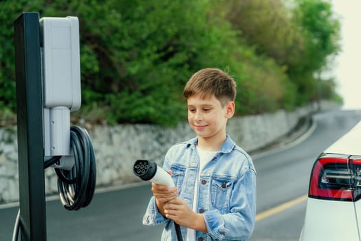 Little boy recharging eco-friendly electric car from EV charging station. EV car road trip travel concept for alternative transportation powered by clean renewable and sustainable energy. Perpetual