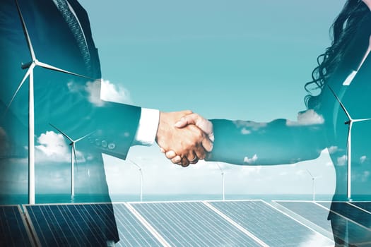 Double exposure graphic of business people handshake over wind turbine farm and green renewable energy worker interface. Concept of sustainability development by alternative energy. uds