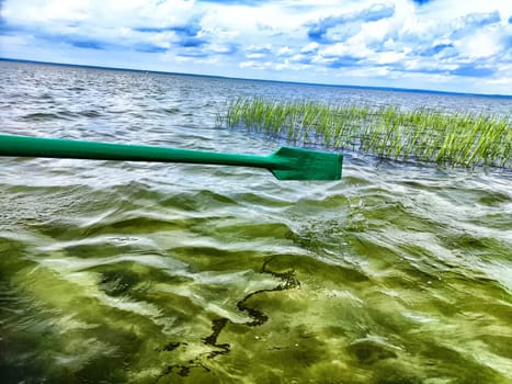 The paddle of a boat and the water of a large lake in the background. Natural landscape, travel, recreation. boat paddle extends over a calm lake