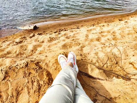 Human feet on sandy beach. The concept of tourism and recreation. Rested legs stretched towards the calm sea