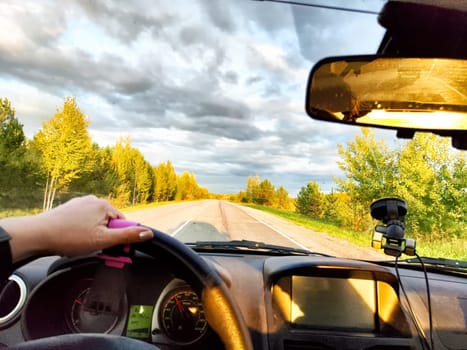 Car salon, windshield, hand of woman on steering wheel and landscape. View from seat of female driver on nature and Road, trees, blue sky at sunny day