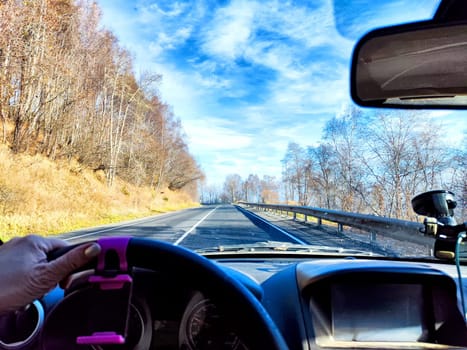 Car salon, windshield, hand of woman on steering wheel and landscape. View from seat of driver on nature landscape. Single trip of female traveler