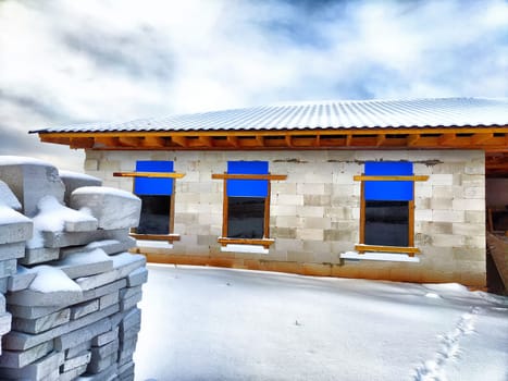 An unfinished house and building materials in the snow. Building a new house in winter. An unfinished house with building materials surrounded by snow