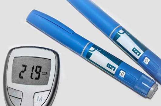 Blood sugar meter with test strips indicates high blood sugar levels and injection pen for diabetes. High quality photo