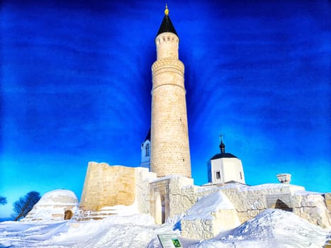 An old mosque with a minaret in winter. The concept of travel. Snow-covered mosque with towering minaret against a bright sky