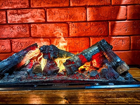 Fireplace. Firebrands, fire and a brick wall on the background. Firebrands ablaze with a cozy flame against a brick backdrop