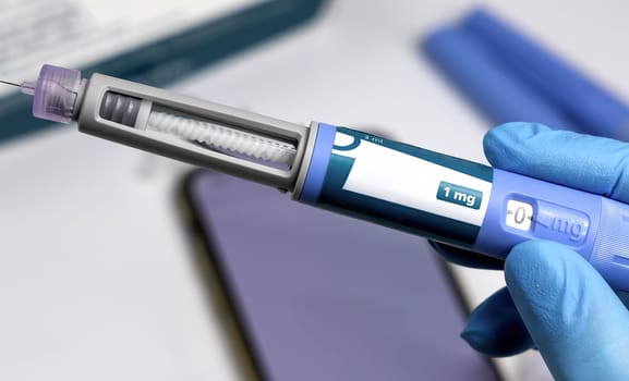 Hands in blue surgical gloves holding Ozempic Insulin injection pen for diabetics.