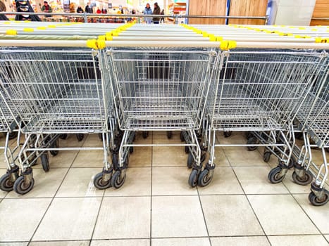 Grocery baskets on wheels in the store. Row of Metal Shopping Baskets on Wheels Inside a Grocery Store. Metal shopping carts lined up at a grocery