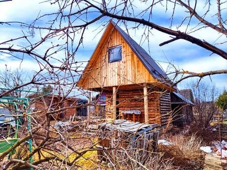 An old wooden house through bare branches of trees. Construction of new house. Rustic wooden house seen through bare tree branches under construction