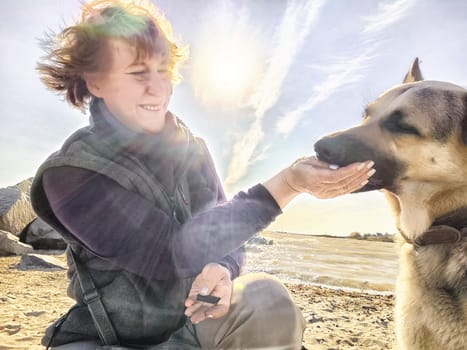 A girl treats a German Shepherd dog in nature with sun. Mature middle aged woman with pet