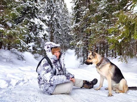 Adult girl or mature lady with shepherd dog in winter nature landscape in forest. Middle aged woman training big shepherd dog in cold day. Friendship, love, communication, fun, hugs