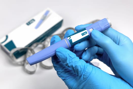 Hands in blue surgical gloves holding Ozempic Insulin injection pen for diabetics.