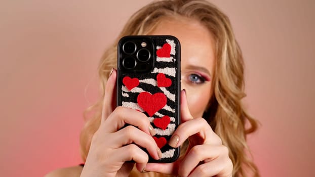 A young woman with red lipstick takes a selfie with long blond hair and makeup. The girl is smiling and looking at the camera close-up