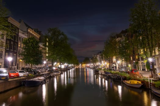 Netherlands. Summer night on the embankment of Amsterdam. Parked cars and lamps on embankments. Boats moored along the banks of the canal
