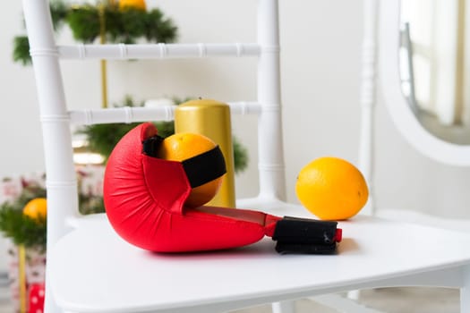 Sports equipment: dumbbell, boxing gloves, fir branch, Christmas ornament, gifts on a chair.