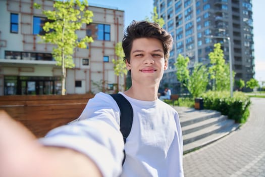 Selfie portrait of young happy handsome man with curly hair, guy university college student outdoor. Youth, urban style, 19,20 years male, lifestyle concept