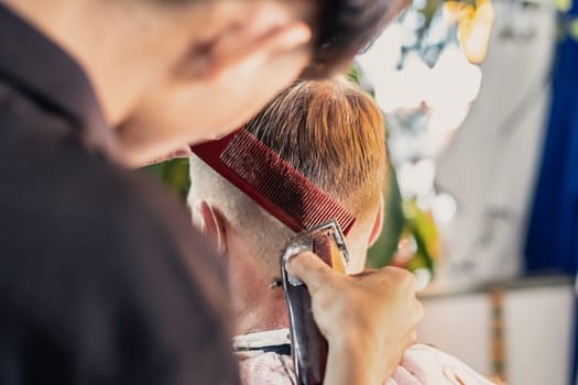 Neat young Vietnamese hairdresser makes haircut to male. Back view. Professional skills.