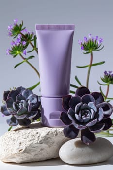A small purple tube of lotion sits on a rock next to purple flowers. The flowers are purple and green, and they are arranged in a way that makes the lotion tube stand out
