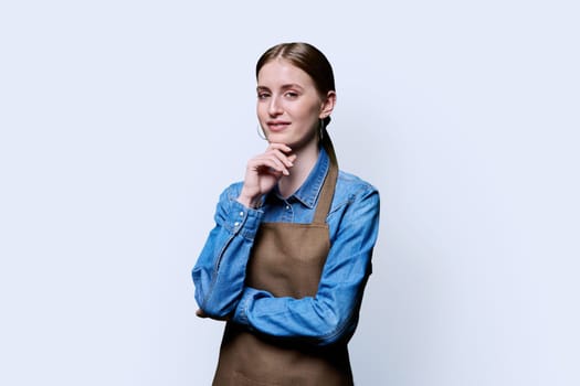 Portrait of young smiling confident woman in apron on white studio background. Successful positive female looking at camera. Worker, startup, small business, service sector, staff, youth concept