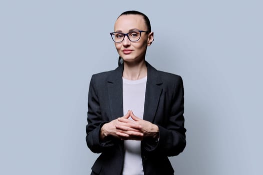 Portrait of thinking serious 30s business woman on grey studio background. Confident female in glasses, suit looking at camera. Business work teaching job career people concept