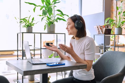 Young woman in headphones having video chat conference call using laptop computer sitting in coworking cafe. Female college student studying online listening webinar preparing exam, working remotely