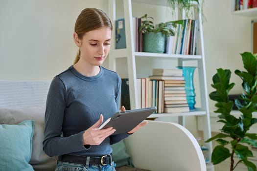 Young female teenager with digital tablet, stylus drawing illustrating sitting on couch at home. Technologies, leisure, creativity, education, freelance work, lifestyle, youth concept