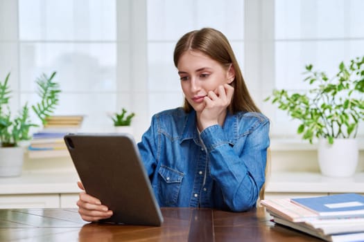 Young teenage female student sitting at home looking talking in web camera of digital tablet. Girl teenager 16,17,18 years old studying remotely, video conference call, e-learning technology education