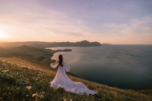 A woman in a white dress stands on a hill overlooking a body of water. The scene is serene and peaceful, with the woman's dress billowing in the wind. The combination of the woman's elegant attire