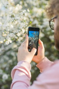 Man holding mobile phone and take photo blooming spring cherry and apples trees in sunlight. Smartphone photo for social media. Copy space.