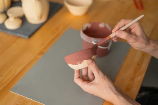 Close-up of a potter's hands with a brush painting ceramic dishes