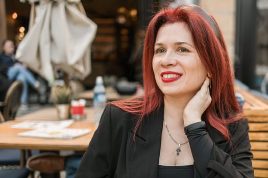 Beautiful happy woman with long red hair enjoying pasta in a street cafe