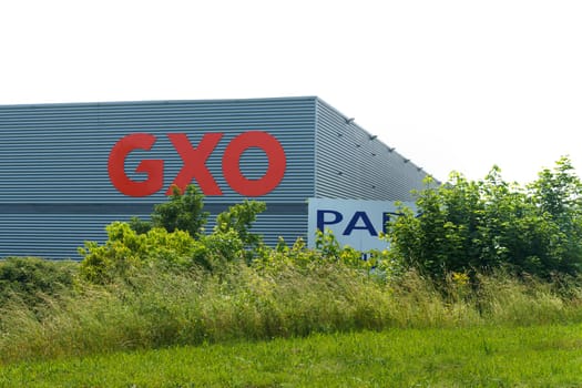 Lyon, France - May 30, 2023: The facade of a GXO logistics warehouse surrounded by lush greenery under a bright blue sky.