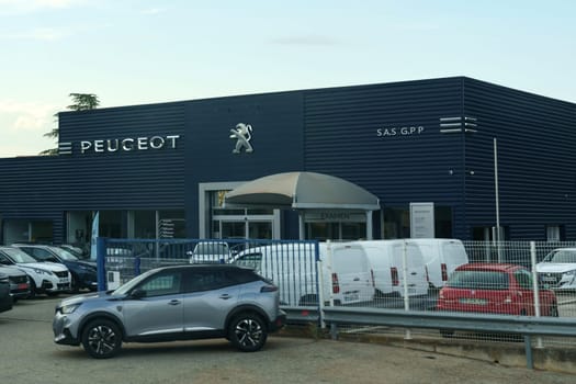 Montelimar, France - May 30, 2023:The facade of a Peugeot car dealership with a selection of cars parked in front, twilight sky indicating evening hours.