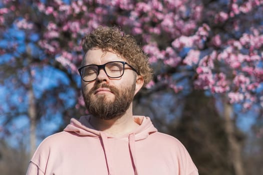 Man allergic enjoying after treatment from seasonal allergy at spring. Portrait of happy bearded man smiling in front of blossom tree at springtime. Spring blooming and allergy concept. Copy space.