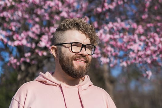 Man allergic enjoying after treatment from seasonal allergy at spring. Portrait of happy bearded man smiling in front of blossom tree at springtime. Spring blooming and allergy concept. Copy space.