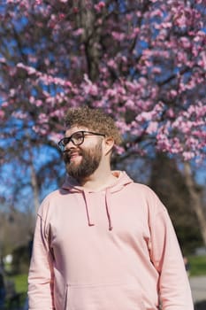 Man allergic enjoying after treatment from seasonal allergy at spring. Portrait of happy bearded man smiling in front of blossom tree at springtime. Spring blooming and allergy concept. Copy space.