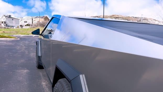 An up-close look at the distinctive, sharp angles of the Tesla Cybertruck’s design, focusing on the sleek roofline and robust structure, set against a suburban background with a clear sky.