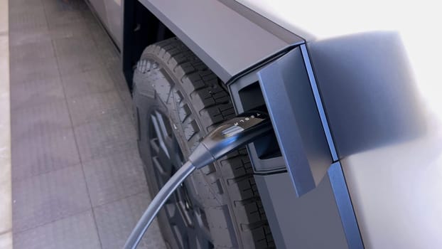 This image showcases the charging connector of a Tesla Cybertruck securely plugged into its port, highlighted by the green indicator lights, signifying active charging status in a close-up view.