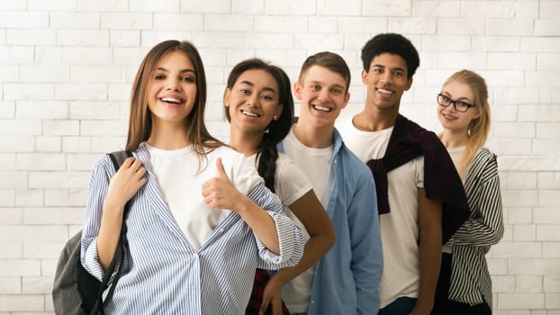 A diverse group of multiethnic teenagers is lined up, displaying a variety of cheerful expressions. The backdrop features a white brick wall, suggesting an informal or educational setting