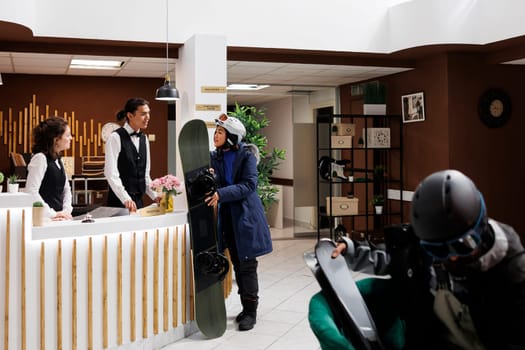 Female customer awaits check-in at luxurious ski resort ready for winter holiday filled with snowboarding and relaxation. Hotel receptionists providing exceptional services to woman at front desk.