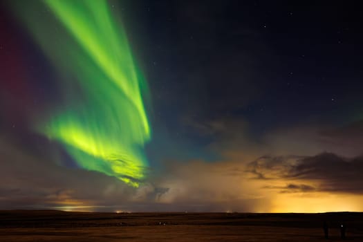 Aurora borealis appears over icy landscape and glittering night sky of Iceland. Arctic northern lights creating enchanting winter scenery with shades of green and gold, natural phenomenon.