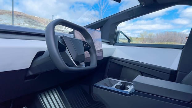 A driver perspective inside the Tesla Cybertruck, highlighting its spacious, minimalist interior with a large touchscreen display and futuristic steering wheel, set against a backdrop of a scenic landscape.