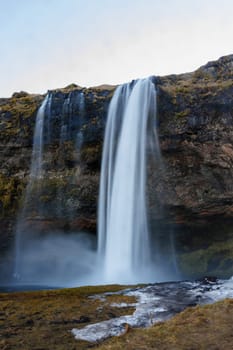 Water flow from icelandic stones forming nordic waterfall and falling down hill. Scandinavian magnificent seljalandsfoss cascade sits in a wintry setting and illustrating arctic nature.