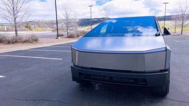 Denver, Colorado, USA-April 28, 2024- This image highlights the bold, angular front design of a Tesla Cybertruck, showcasing its innovative structure and reflective surface, parked in a spacious outdoor lot under a cloudy sky.