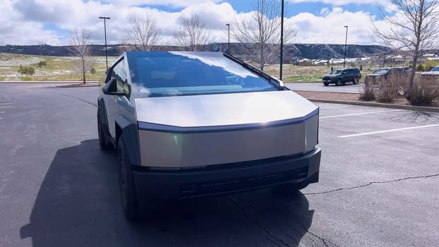 Denver, Colorado, USA-April 28, 2024- This image highlights the bold, angular front design of a Tesla Cybertruck, showcasing its innovative structure and reflective surface, parked in a spacious outdoor lot under a cloudy sky.