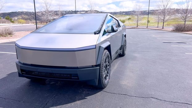 Denver, Colorado, USA-April 28, 2024- This image highlights the bold, angular front design of a Tesla Cybertruck, showcasing its innovative structure and reflective surface, parked in a spacious outdoor lot under a cloudy sky.
