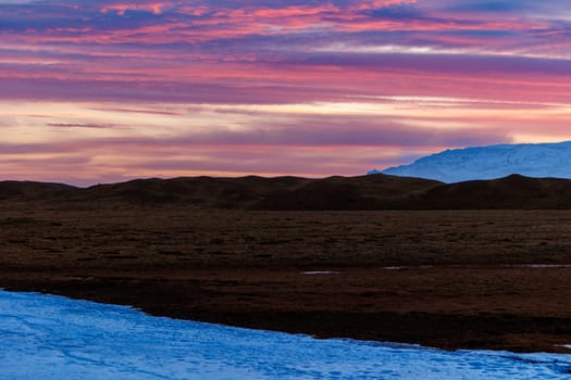 Spectacular sunset near frosty hills in iceland, night photography concept. Majestic icelandic landscapes with sun setting over fields, creating amazing view of pink cotton candy sky.
