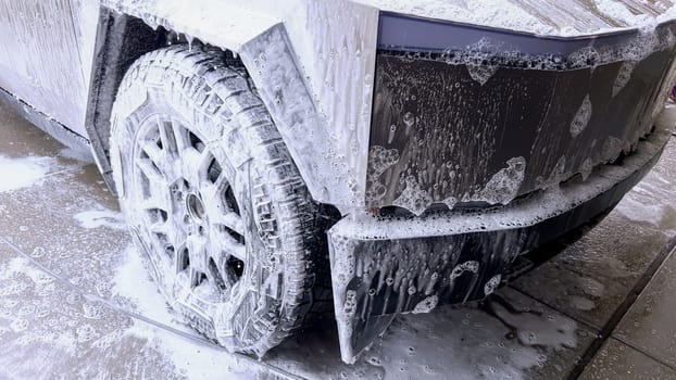 A Tesla Cybertruck undergoes a thorough wash, its unique and angular exterior covered in soap suds, highlighting the vehicle sleek design and durable surfaces.